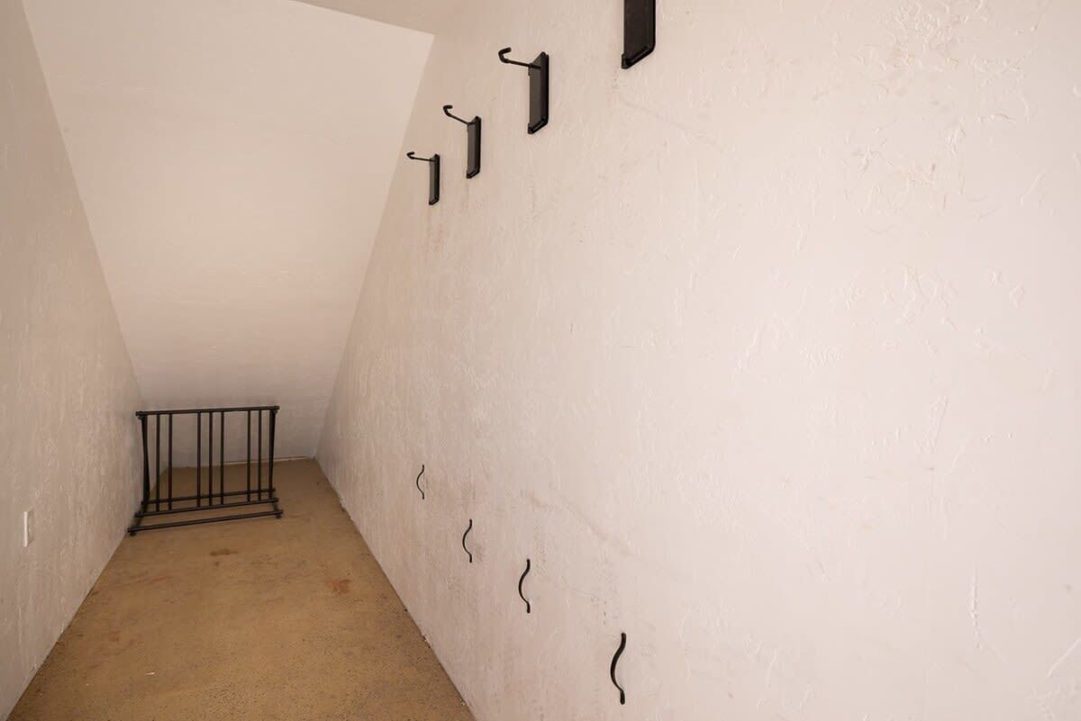 A narrow hallway with a metal railing, white walls, and a sloped ceiling.