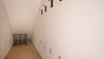 A narrow hallway with a metal railing, white walls, and a sloped ceiling.