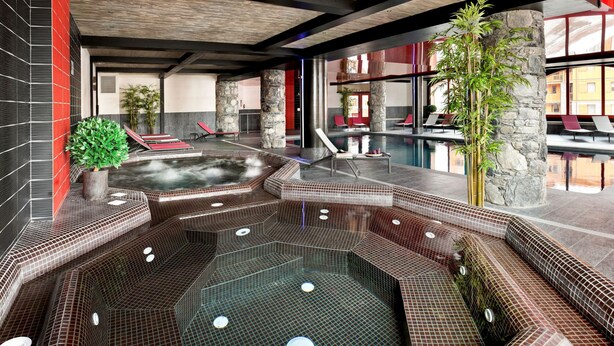 Un espace piscine intérieur moderne, doté d’un jacuzzi, de chaises longues et d’un pilier en pierre.