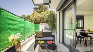 A balcony with wicker furniture, a glass table with fruit, and a green screen. - MAMAD - Bahai Serenity Apartment by Sea N' Rent (Haifa)