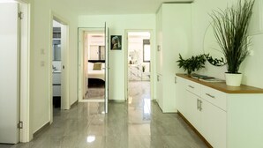 A hallway with a marble floor, white walls, and a wooden counter with a plant. - MAMAD - Bahai Serenity Apartment by Sea N' Rent (Haifa)