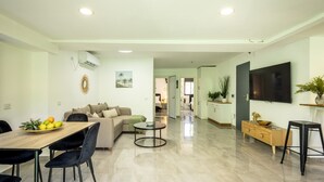 A modern living room with a dining area, a sofa, a coffee table, and a TV mounted on the wall. - MAMAD - Bahai Serenity Apartment by Sea N' Rent (Haifa)