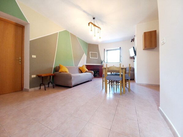 A modern living room with a sofa, a wooden dining table, and a television mounted on the wall.