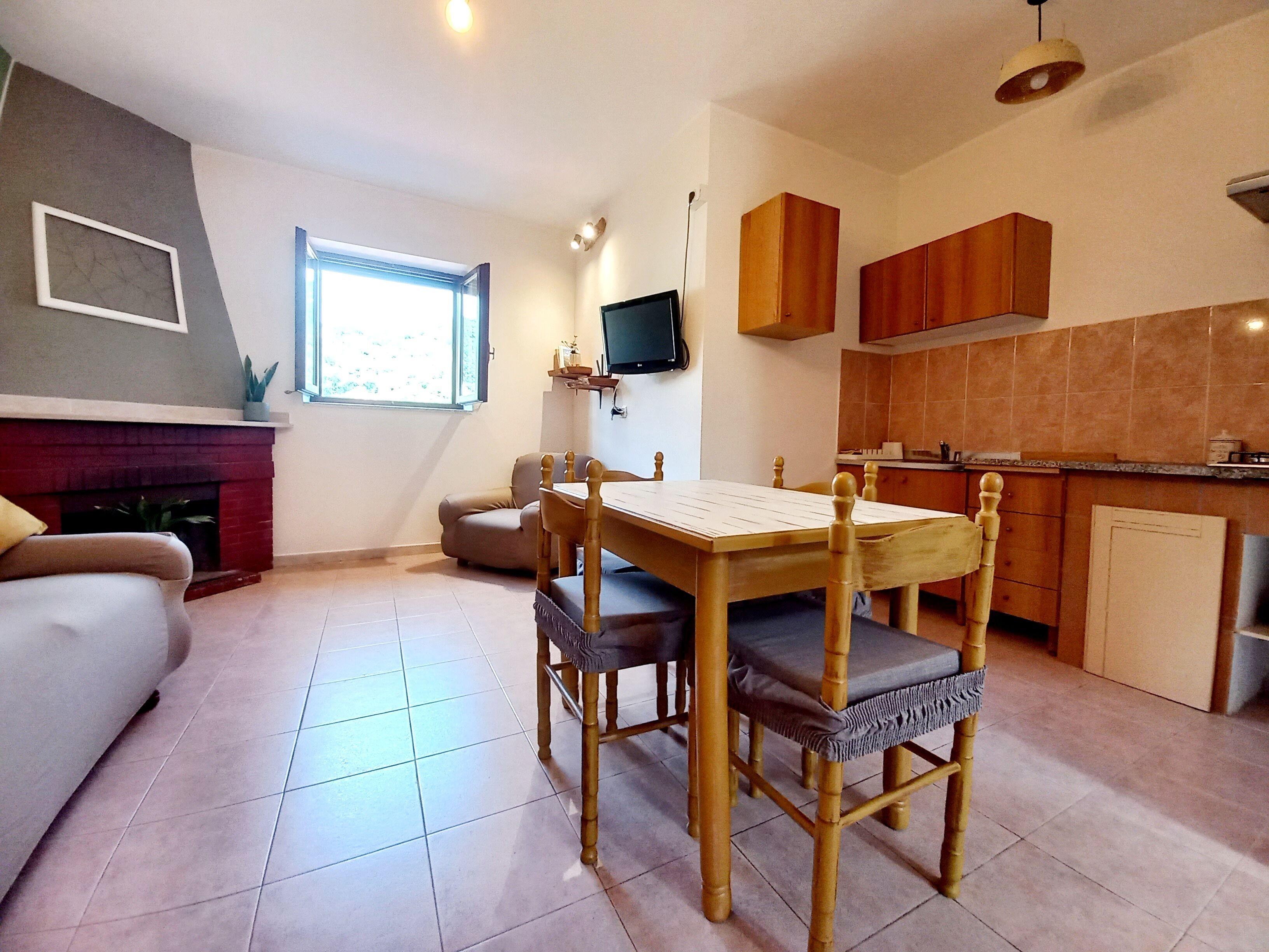 Un espacio habitable compacto con mesa y sillas, sofá, chimenea, televisor y  área de cocina.