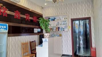 A reception area with a reception desk, a chair, a potted plant, and a wall-mounted shelf with various items.