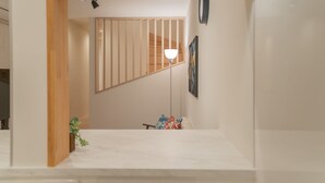 Un interno moderno con struttura a travi in legno, una scala, una lampada da terra e una piccola pianta.