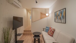 Un soggiorno moderno con una TV a schermo piatto, un tavolino rotondo, un divano con cuscini decorati, una scala e un condizionatore d'aria a parete.