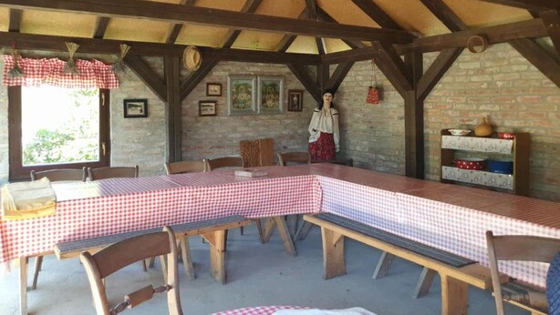 A rustic dining area with a long table covered in checkered tablecloths, wooden benches, and a brick wall backdrop. - Apartment Čeliković (Draz)