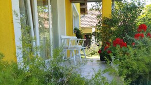 A yellow building with a covered porch, a white chair, and red flowers. - Apartment Čeliković (Draz)