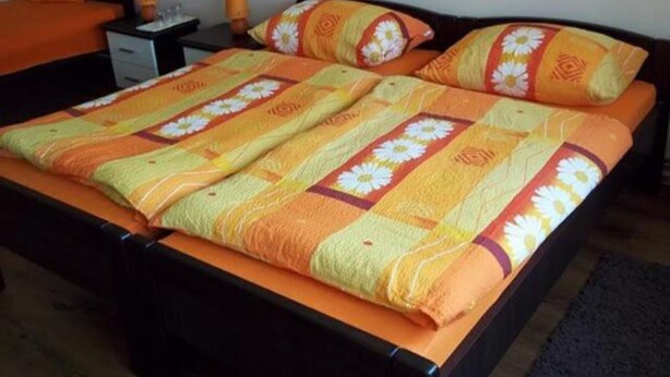 A bed with a floral bedspread and matching pillows, a nightstand with a lamp, and an orange chair.