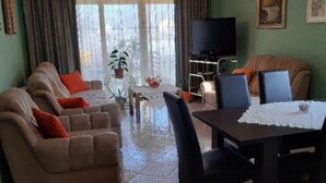 A living room with a sofa set, a dining table with chairs, a television, and a potted plant. - Apartment Čeliković (Draz)