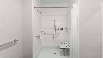 A modern, accessible shower area with a glass door, a handrail, a showerhead, and a handheld shower attachment.