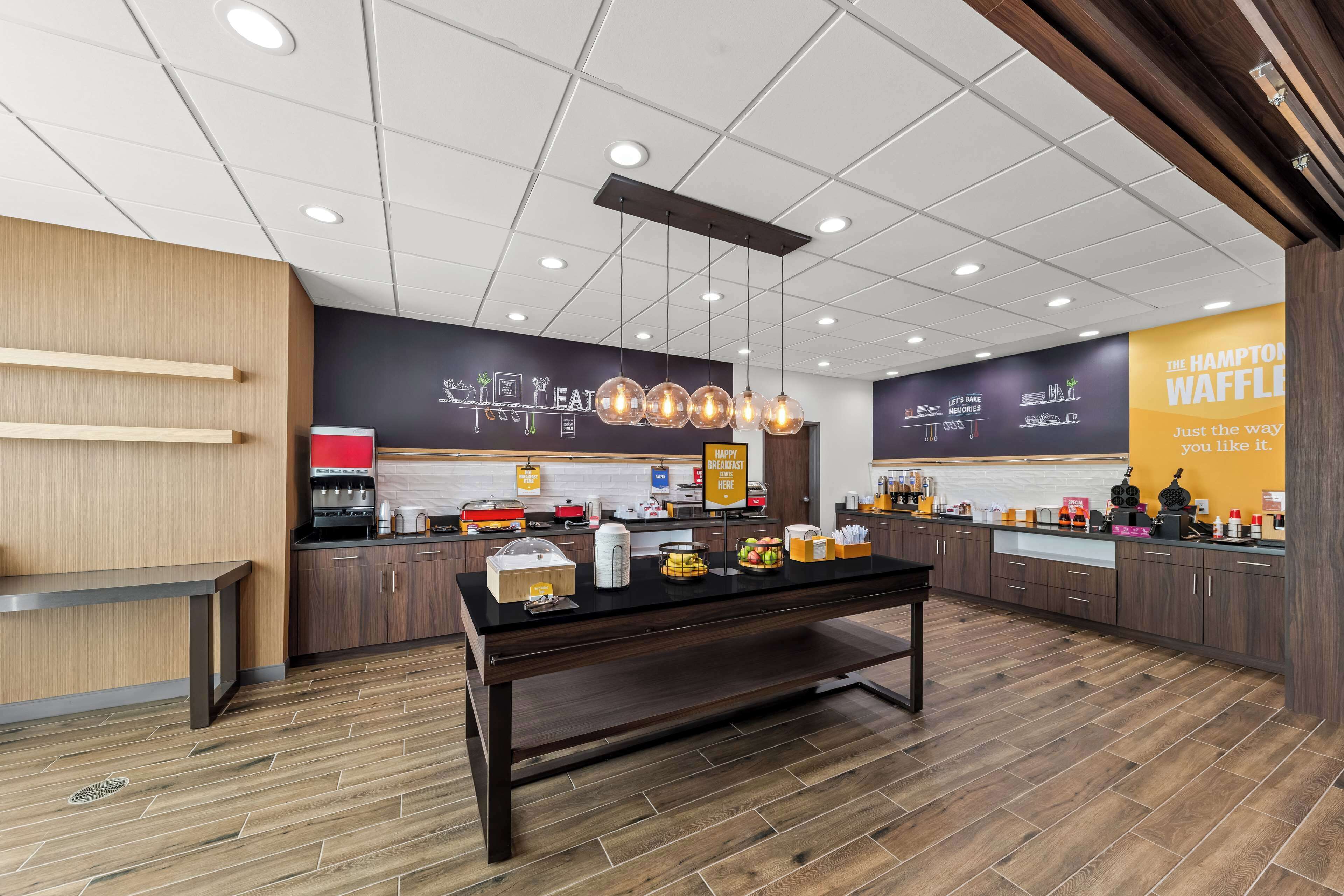 A modern kitchen area with a central island, wooden cabinets, and a variety of breakfast items displayed on the counter.