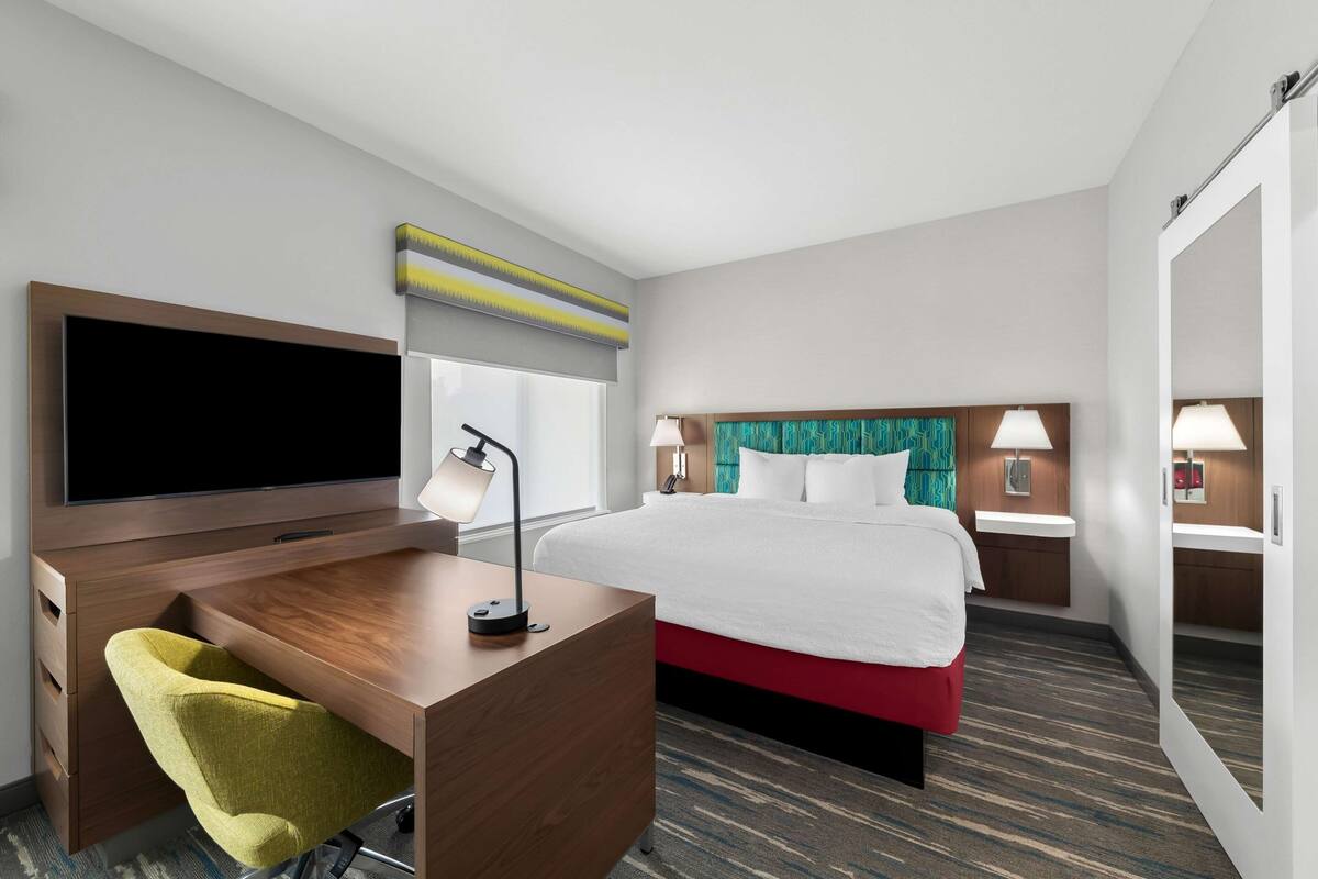 Una habitación de hotel con cama, escritorio, silla, televisor y dos lámparas de noche.