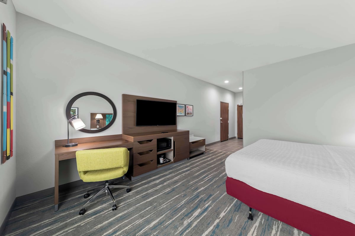 Una habitación de hotel con cama, escritorio con silla, televisor y espejo.
