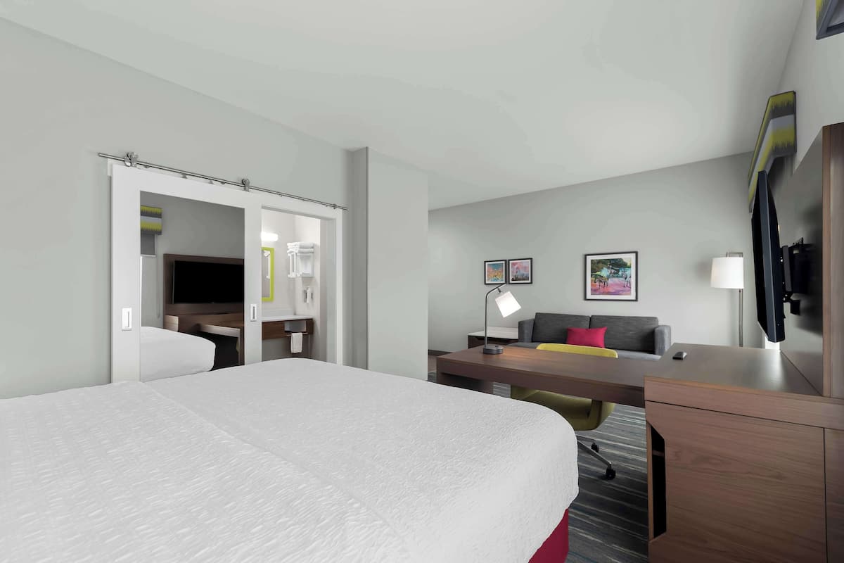 Habitación de hotel con una cama grande, un escritorio con silla, un sofá, un televisor y una lámpara de escritorio.