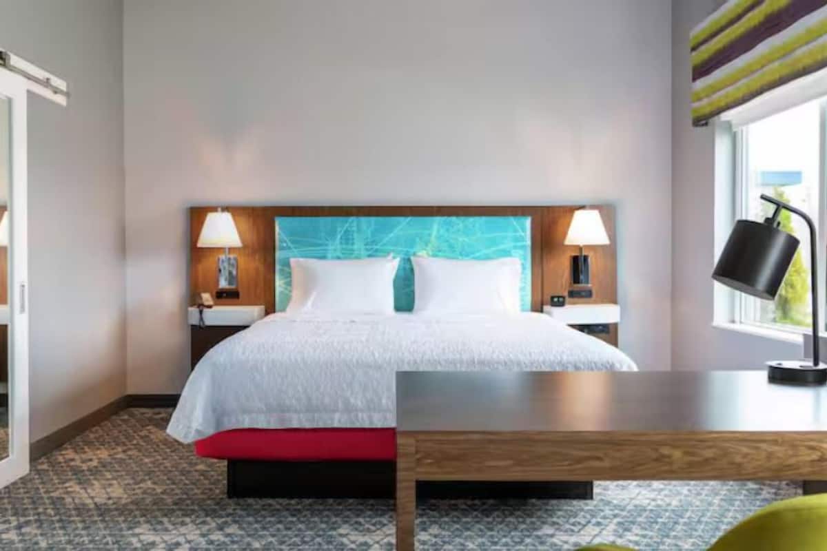 Una habitación de hotel con cama, mesitas de noche, un escritorio y una ventana.