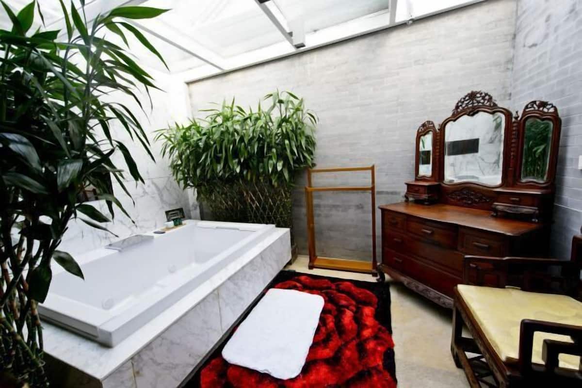 A bathroom with a bathtub, a wooden vanity with a mirror, and a large potted plant.