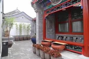 Un edificio tradicional con fachada roja, ventanas grandes y plantas en macetas afuera.