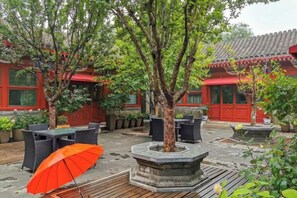 An outdoor courtyard with traditional architecture, including red doors and tiled roofs, surrounded by potted plants and outdoor furniture. - Ancient City Old Courtyard Boutique Hotel (Beijing)