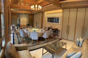 A dining area with a round table, chairs, and a chandelier. There is a sofa and a coffee table in the foreground. - Ancient City Old Courtyard Boutique Hotel (Beijing)