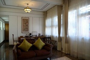 A room with a brown sofa, a dining table, and chairs. There is a painting on the wall and a window with curtains. - Ancient City Old Courtyard Boutique Hotel (Beijing)