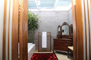 Un baño con tocador de madera, un espejo, perchero para toallas y una planta.