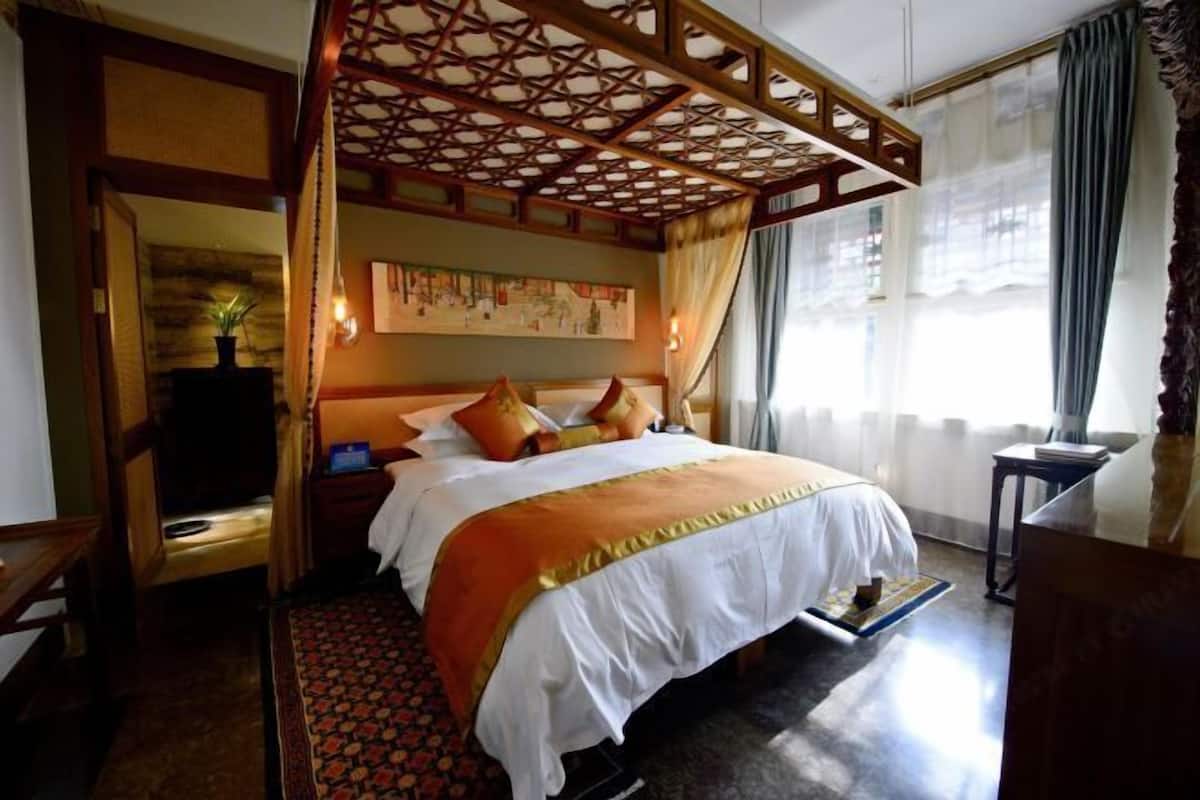 A hotel room with a bed, a nightstand, a desk, a chair, a window with curtains, and a decorative ceiling.