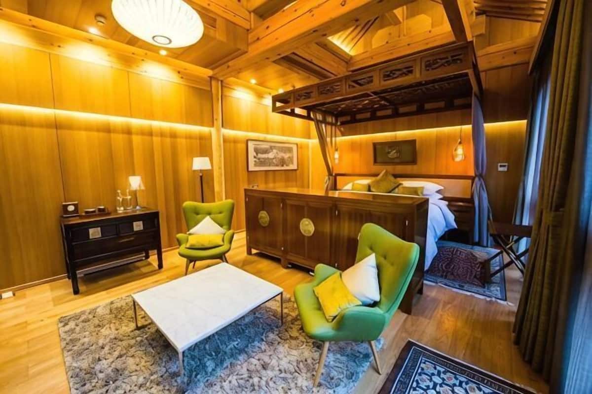 A wooden interior with a bed, two armchairs, a nightstand, and a small table.