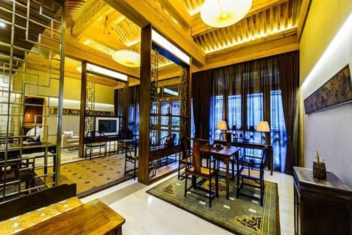 A hotel room with a wooden ceiling, a dining area with chairs and a table, and a large window with curtains.