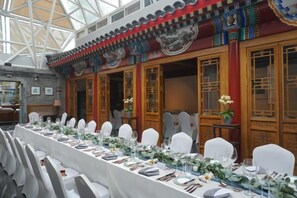 A banquet hall with a long table set for a formal event, traditional wooden doors, and a high ceiling with a glass structure. - Ancient City Old Courtyard Boutique Hotel (Beijing)