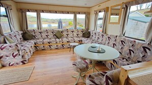 A cozy RV interior with a large sofa, a small table, and a view of a lake. - Mobile Home - Sleeps 6 - Pets Ok - Parking (Birra)