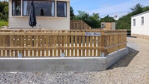 A mobile home with a fenced deck labeled "Ella Rose," a satellite dish, and a small shed. - Mobile Home - Sleeps 6 - Pets Ok - Parking (Birra)