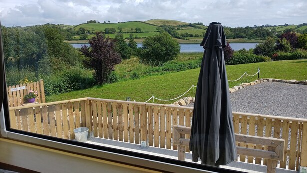 A view from a window overlooking a grassy area with a wooden fence, a bench, and a sign that reads "Ballet-Magpie." - Mobile Home - Sleeps 6 - Pets Ok - Parking (Birra)