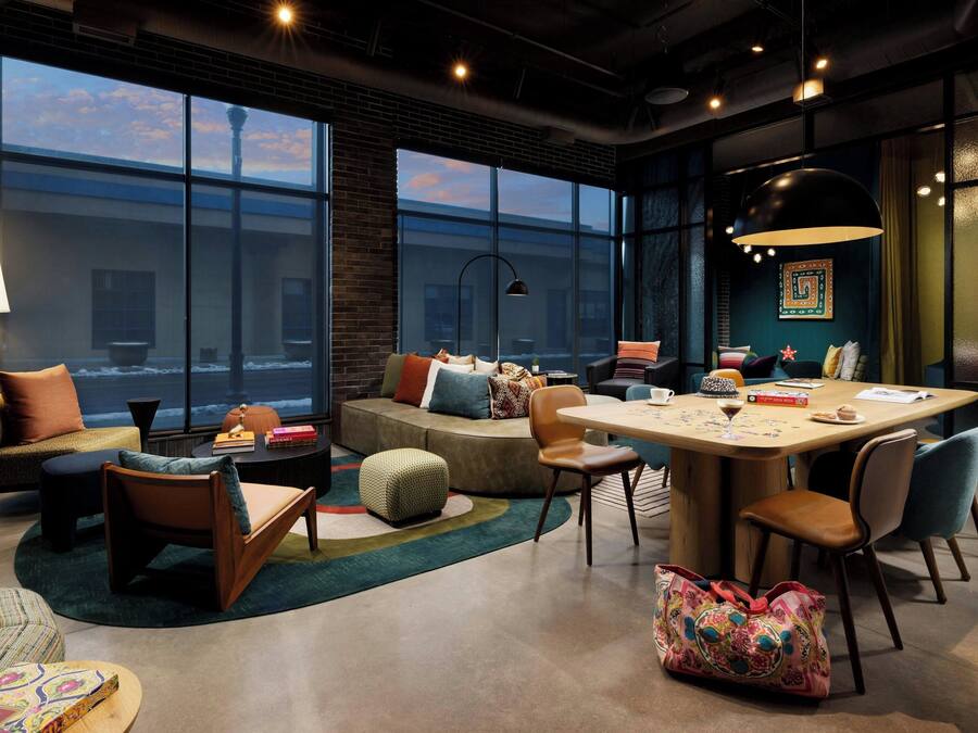 A modern hotel room with a large window, a round table, and comfortable seating.