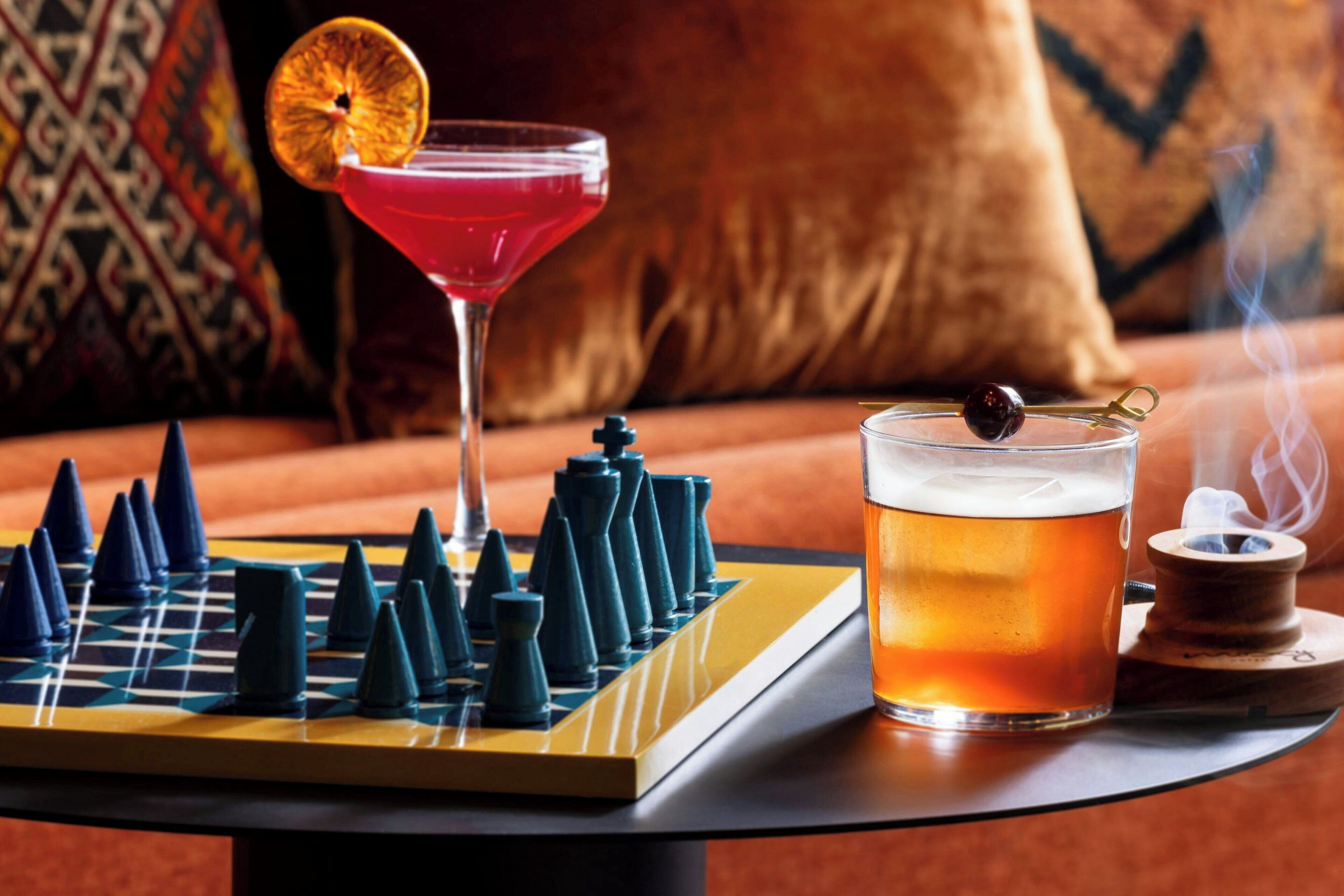 A chessboard, a cocktail, and a smoking device on a table.