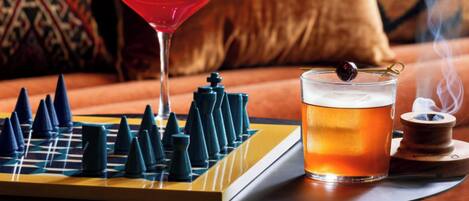Ein Schachbrett, ein Cocktail und ein Räuchergerät auf einer Tischplatte.