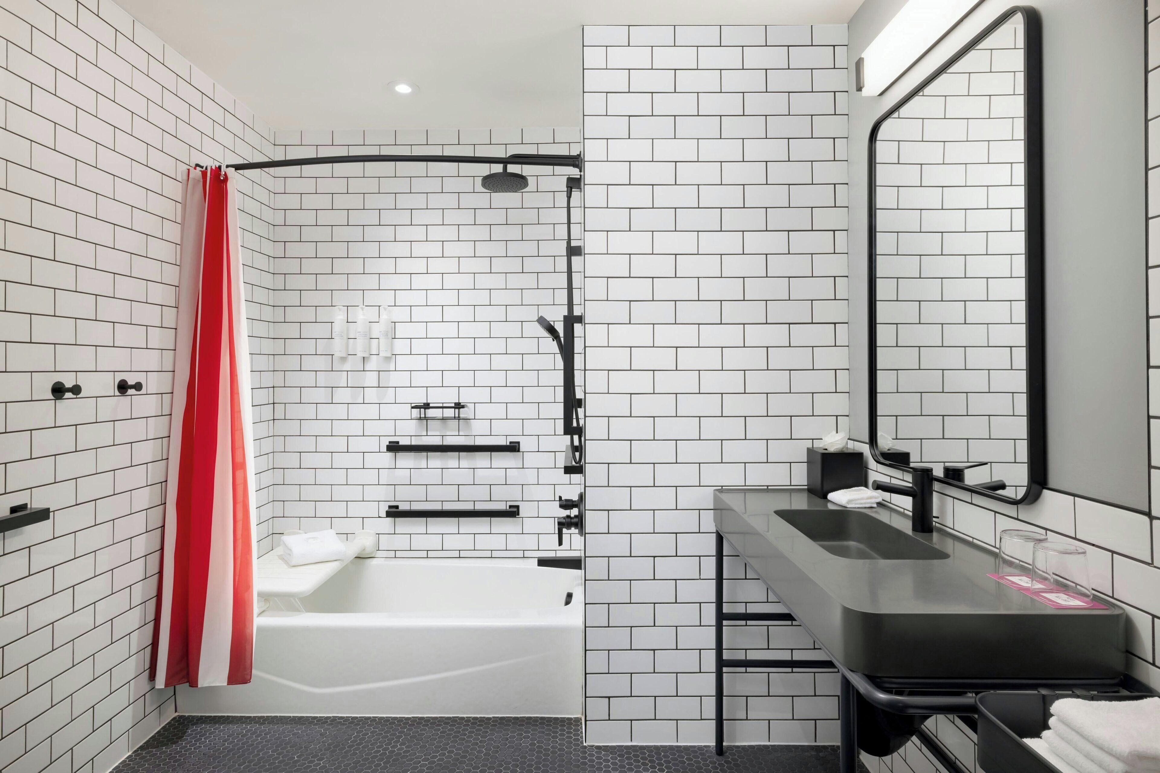 A modern bathroom with white subway tiles, a black bathtub, a black vanity, and a red shower curtain.
