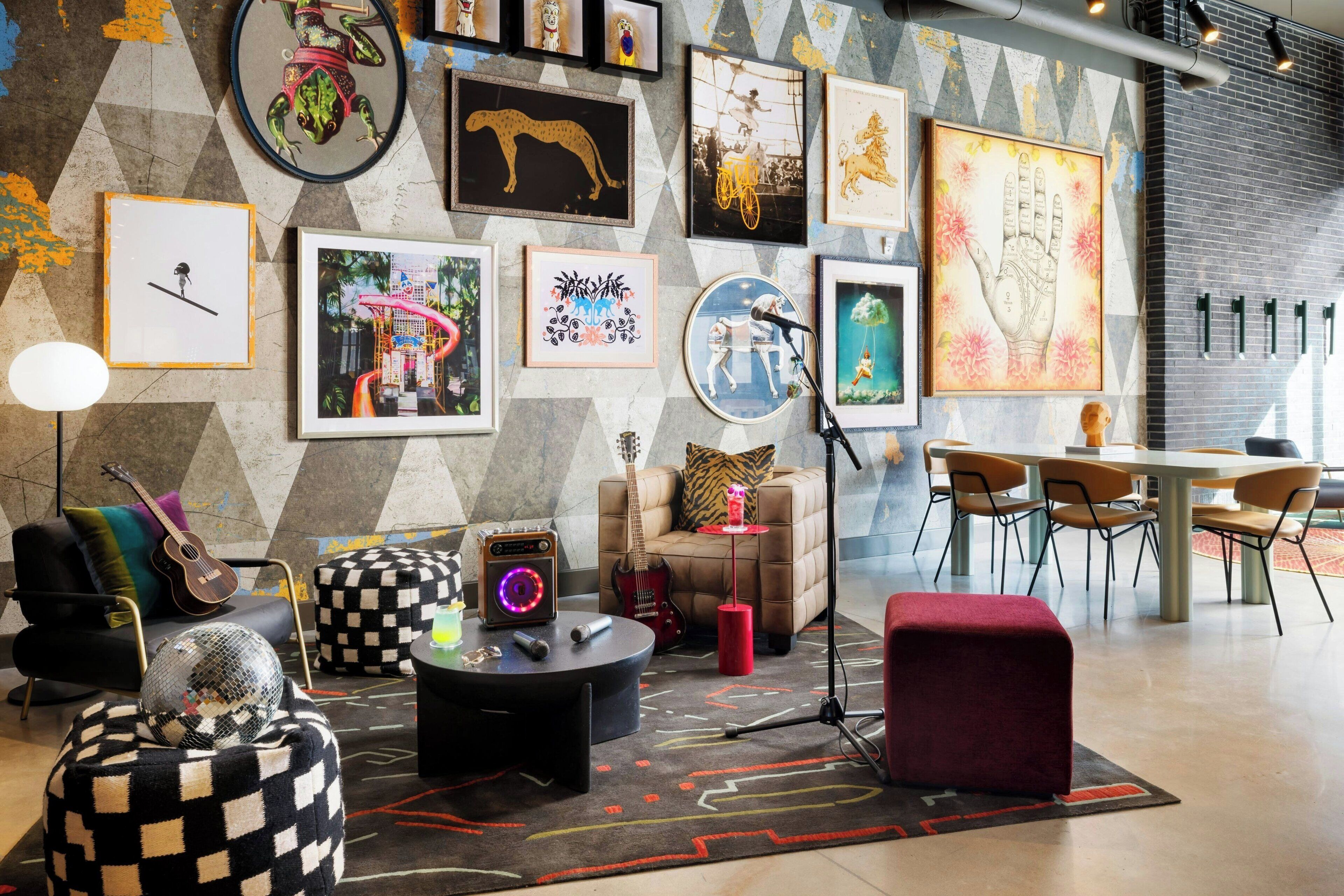 A modern living room with a geometric wall design, a variety of framed artworks, a guitar, a disco ball, and a red ottoman.