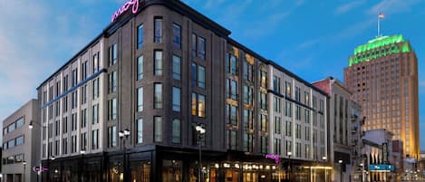 A modern hotel with a prominent neon sign, large windows, and a corner location.