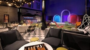 Ein Sitzbereich im Freien mit Schachbrettmuster-Boden, Lounge-Stühlen und einer Feuerstelle.