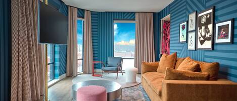 Ein modernes Wohnzimmer mit großem Fenster, Flachbildfernseher, Sofa, Couchtisch und einem gemusterten Teppich.