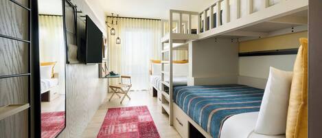 A compact hotel room with a bunk bed, a desk with a chair, a TV mounted on the wall, and a red rug on the floor.