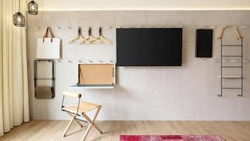 A minimalist room with a large black TV, wooden floor, a red rug, and a folding chair.
