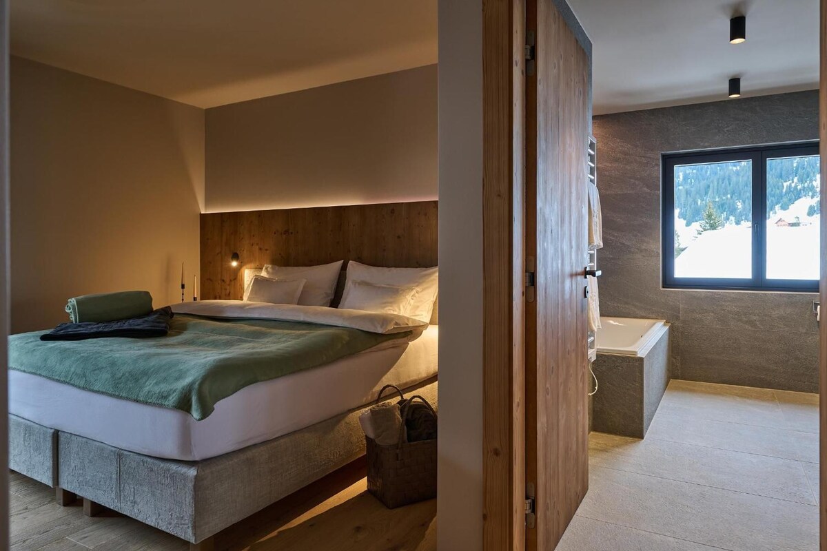 A bedroom with a bed, bedside table, and a window with a view of a snowy landscape.