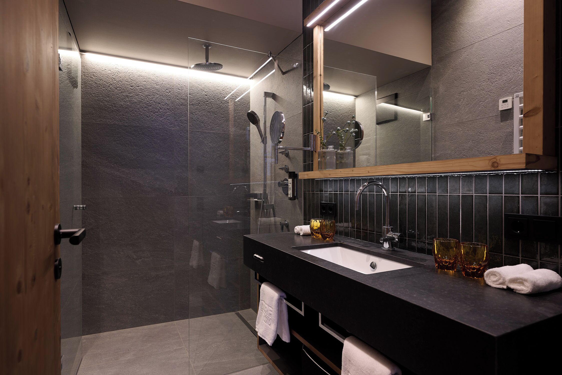 A modern bathroom with a glass-enclosed shower, a black sink, and a large mirror.