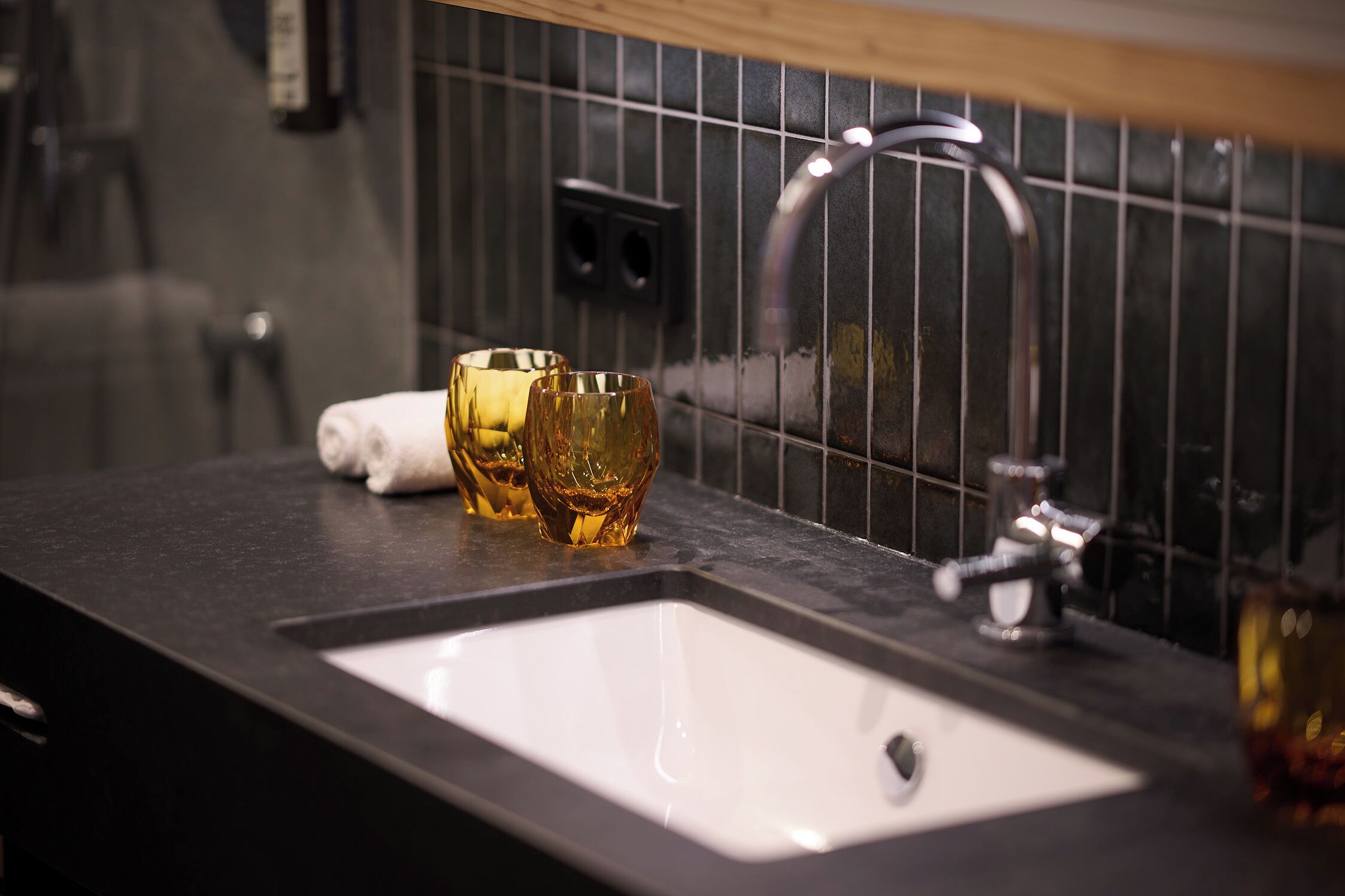 A bathroom with a black tiled wall, a white sink, and two glasses on the counter.