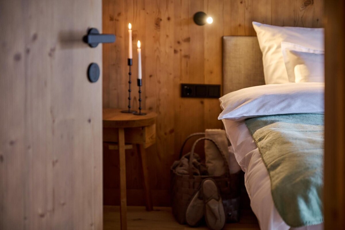 A wooden room with a bed, a small table with candles, and a wall-mounted light fixture.
