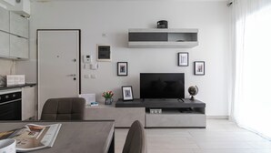 A modern living room with a flat-screen TV, a coffee table, and a dining area with a table and chairs. - Italianway Comfort - Fara 29 (Milan)