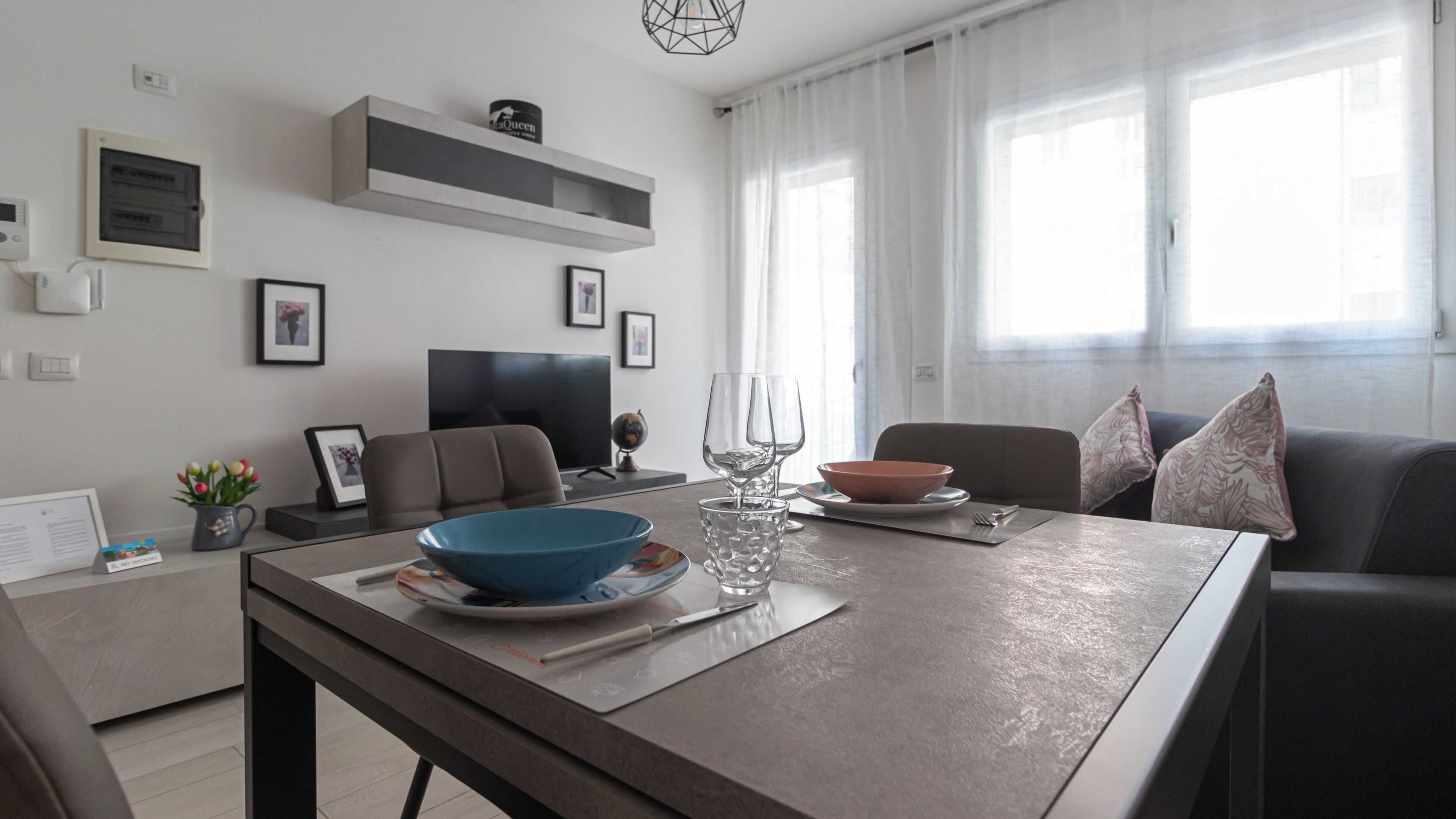 Un soggiorno moderno con zona pranzo, televisione a schermo piatto e una grande finestra con tende leggere.